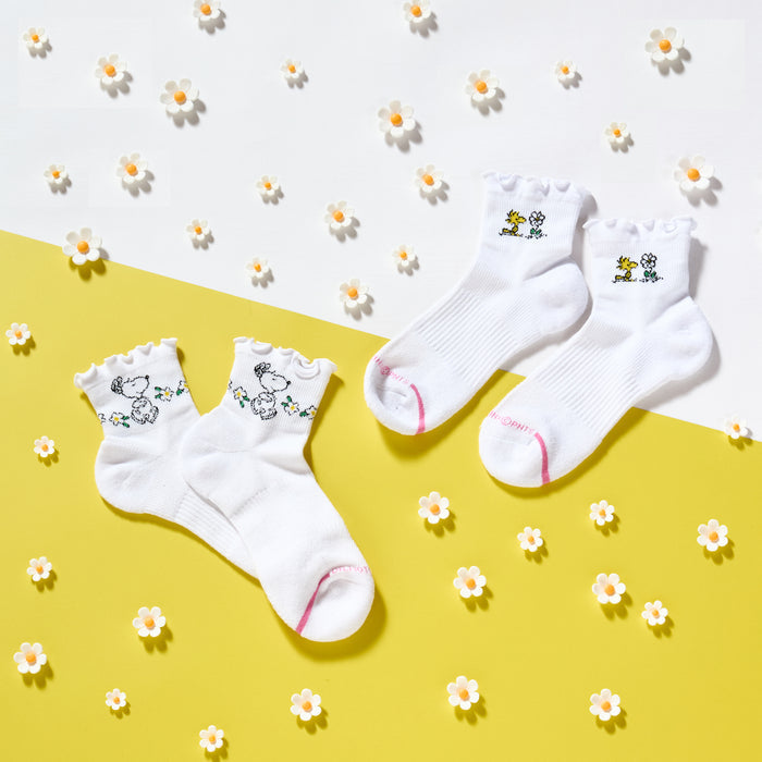 White quarter compression socks with floral lettuce edge and Snoopy designs, displayed on a yellow background with flowers.