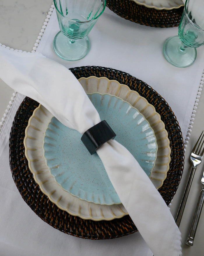 Table setting with a black squared napkin ring holding a white napkin over a blue plate.