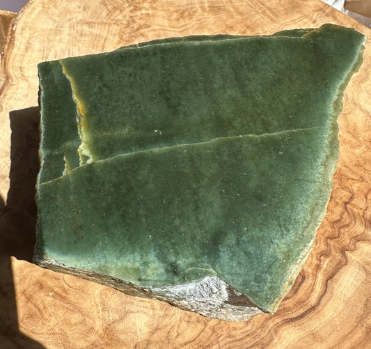 A raw green jade with natural fissures and a rough textured base, displayed on a circular wooden slice.